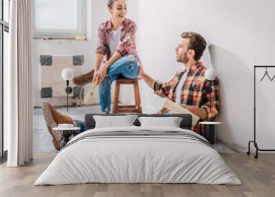 smiling young couple holding paint rollers and talking in new apartment Wall mural