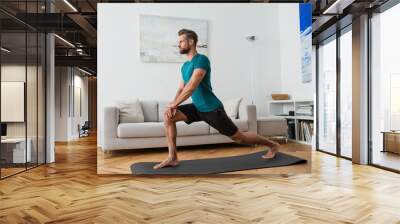 sportive man practicing crescent lunge pose on yoga mat at home Wall mural