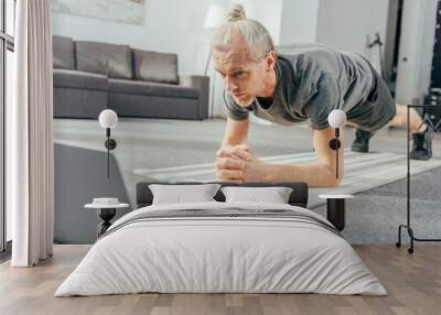 sporty adult man doing plank exercise and looking at laptop Wall mural