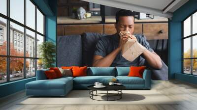 stressed african american man breathing with paper bag while having panic attack at home Wall mural