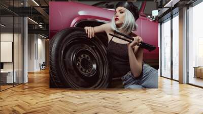 stylish blonde girl in beret leaning at car wheel and looking away while repairing car Wall mural