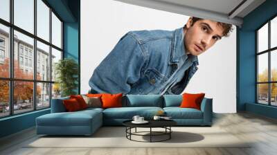 stylish young man in denim clothes posing with hands in pockets and looking at camera isolated on grey. Wall mural