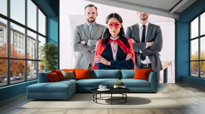 super businesswoman standing with crossed arms in mask and cape with businessmen in office Wall mural