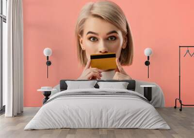 surprised blonde woman covering mouth with credit card isolated on pink Wall mural