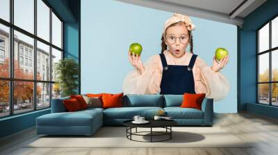 surprised kid in glasses holding green apples isolated on blue Wall mural