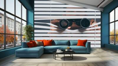 suspicious young man with binoculars spying through blinds Wall mural