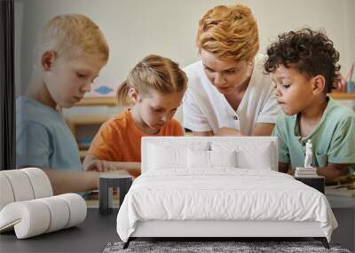 teacher talking to multiethnic kids near didactic materials in montessori school Wall mural