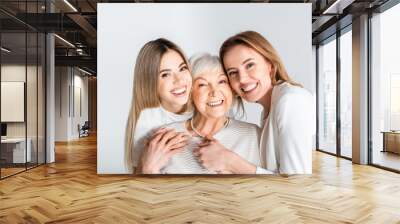 three generation of positive women smiling while looking at camera and hugging isolated on grey Wall mural