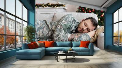 tired bearded man in military uniform sleeping on couch at home on christmas day Wall mural