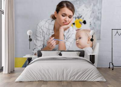 tired woman feeding little son sitting on kids chair Wall mural