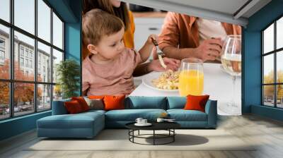 Toddler kid holding fork near parents and pasta in kitchen Wall mural