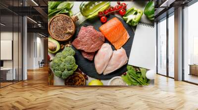 top view of blank notebook near raw meat and fish among fresh vegetables, ketogenic diet menu Wall mural