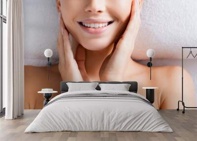 Top view of happy woman touching cheeks and lying on massage table in spa salon, banner Wall mural