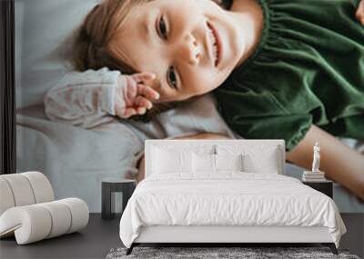 top view of smiling child looking at camera while lying on white bedding near little sister Wall mural