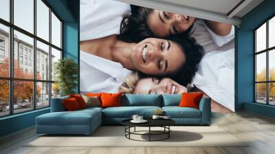 Top view of three smiling multiethnic women in white shirts lying with closed eyes Wall mural