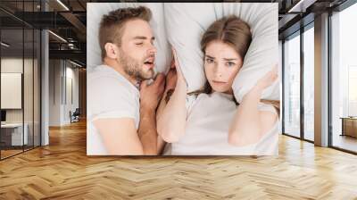 top view of woman plugging ears with pillow while lying in bed near snoring husband Wall mural