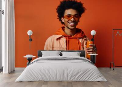 Trendy African American man in orange hoodie holding an orange juice can on vibrant orange background. Wall mural