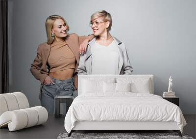 trendy mother and daughter smiling at each other while posing with hands in pockets on grey Wall mural