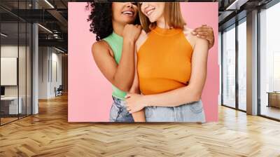 Two attractive diverse women in cozy casual attire hug each other warmly, smiling with joy. Wall mural