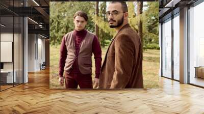 Two handsome men showcase their fashionable autumn attire in a picturesque field surrounded by nature. Wall mural