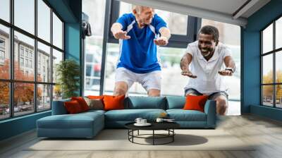 two multicultural mature sportsmen doing squats at gym Wall mural