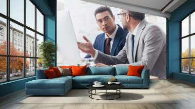 two professional businessmen using desktop computer and discussing project in office Wall mural