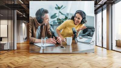 two radio hosts in headphones laughing while recording podcast in studio together Wall mural