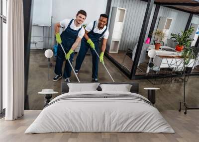 two smiling multicultural cleaners washing floor with mops and looking at camera Wall mural