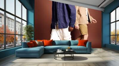 Two young men with stylish attire walking down a brown background. Wall mural