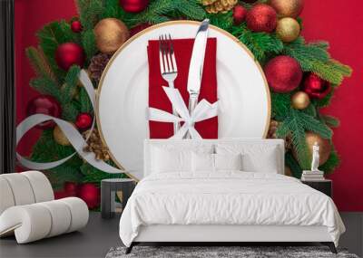 view from above of fork and knife wrapped by festive ribbon on plate surrounded by evergreen tree branches with christmas balls isolated on red Wall mural