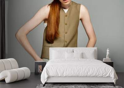 With his striking red hair, a teenager elegantly poses in a stylish smart casual ensemble against grey. Wall mural