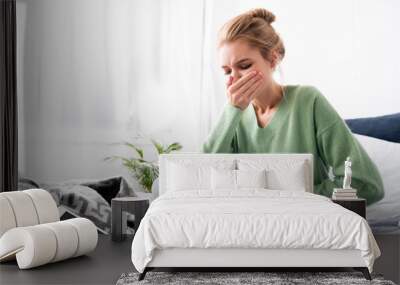 woman having nausea and sitting on bed with digital device Wall mural