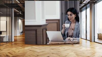 woman holding cup while looking at laptop in restaurant Wall mural