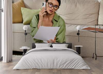 Woman in casual attire chats on cell phone while sitting on floor. Wall mural