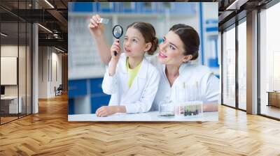 woman teacher and girl student scientists looking at glass microscope slide through magnifier Wall mural