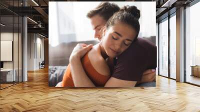 young, tender couple hugging with closed eyes while sitting at home Wall mural