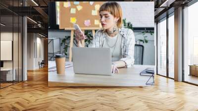 young and stylish businesswoman using cellphone while working near laptop in office, banner Wall mural