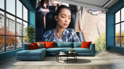 young asian woman sleeping and listening music in earphones during trip on travel bus Wall mural