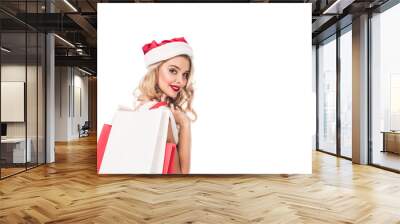 young beautiful woman in christmas hat holding shopping bags over shoulder and looking at camera isolated on white Wall mural