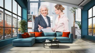 young businesswoman holding document and looking at smiling senior colleague Wall mural