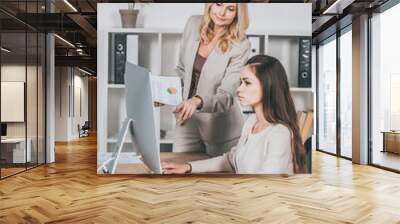 young businesswoman using desktop computer and mature female mentor pointing at screen Wall mural