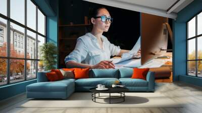 young concentrated asian businesswoman in eyeglasses working with documents and computer Wall mural