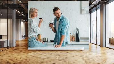 young couple drinking red wine and looking away in kitchen Wall mural