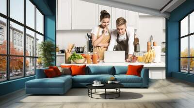 young couple using laptop during cooking in kitchen Wall mural