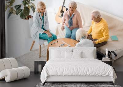 young female nurse playing domino with senior patients in nursing home Wall mural