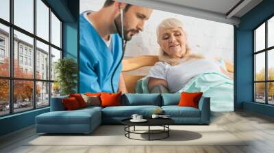 young male nurse measuring blood pressure to senior woman in hospital bed Wall mural