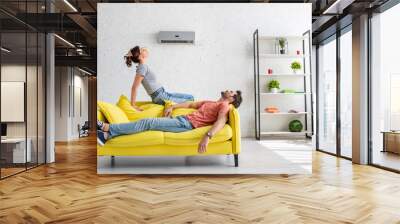 young man and woman resting on yellow sofa under air conditioner at home Wall mural