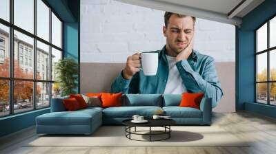 young man holding cup and suffering from toothache Wall mural