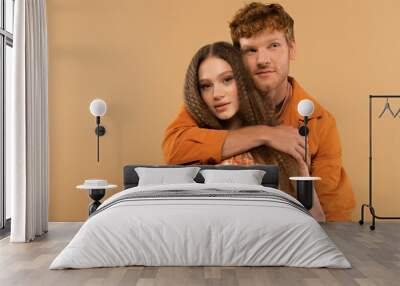 young redhead man hugging girlfriend with wavy hair isolated on beige. Wall mural