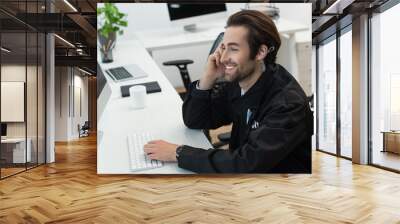 young security man in earphone smiling at workplace near computer monitor. Wall mural